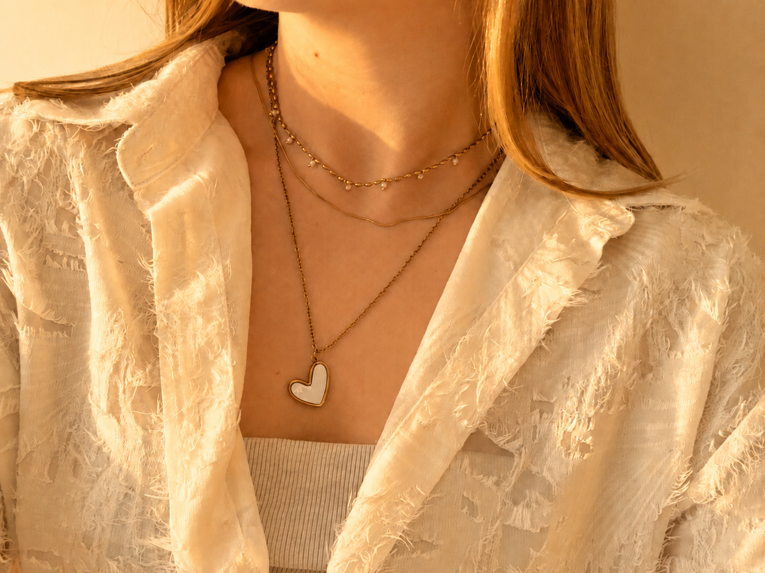 Gelaagde gouden kettingen met hartjeshanger op witte blouse