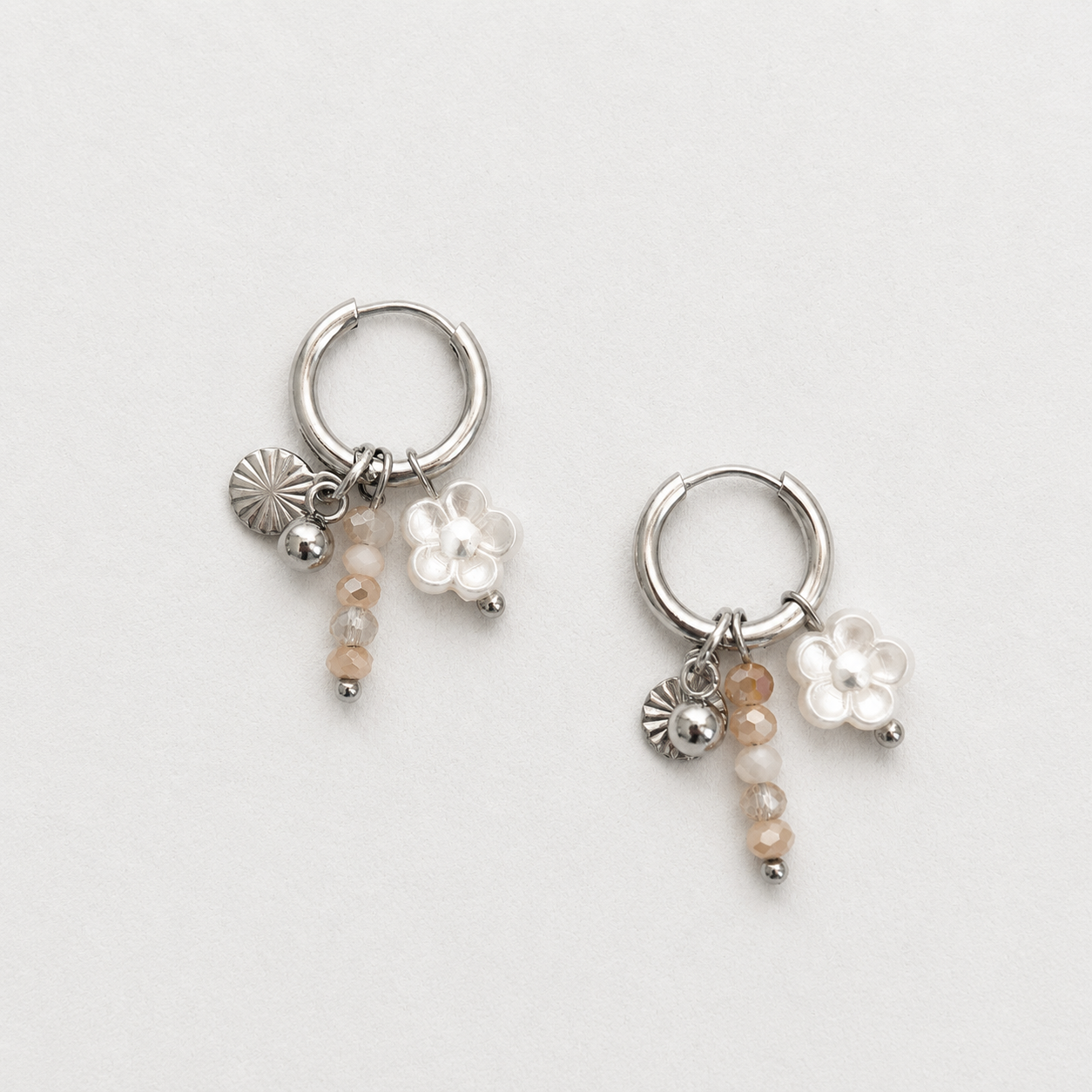 Handgemaakte zilveren RVS oorbellen met transparante witte bloem, beige kristalkralen en zilveren zon-muntje aan kleine zilveren oorring